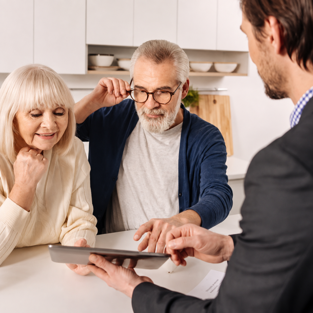 An older couple sits at a table while a Probate Attorney in a suit shows them information on a tablet in a bright kitchen.