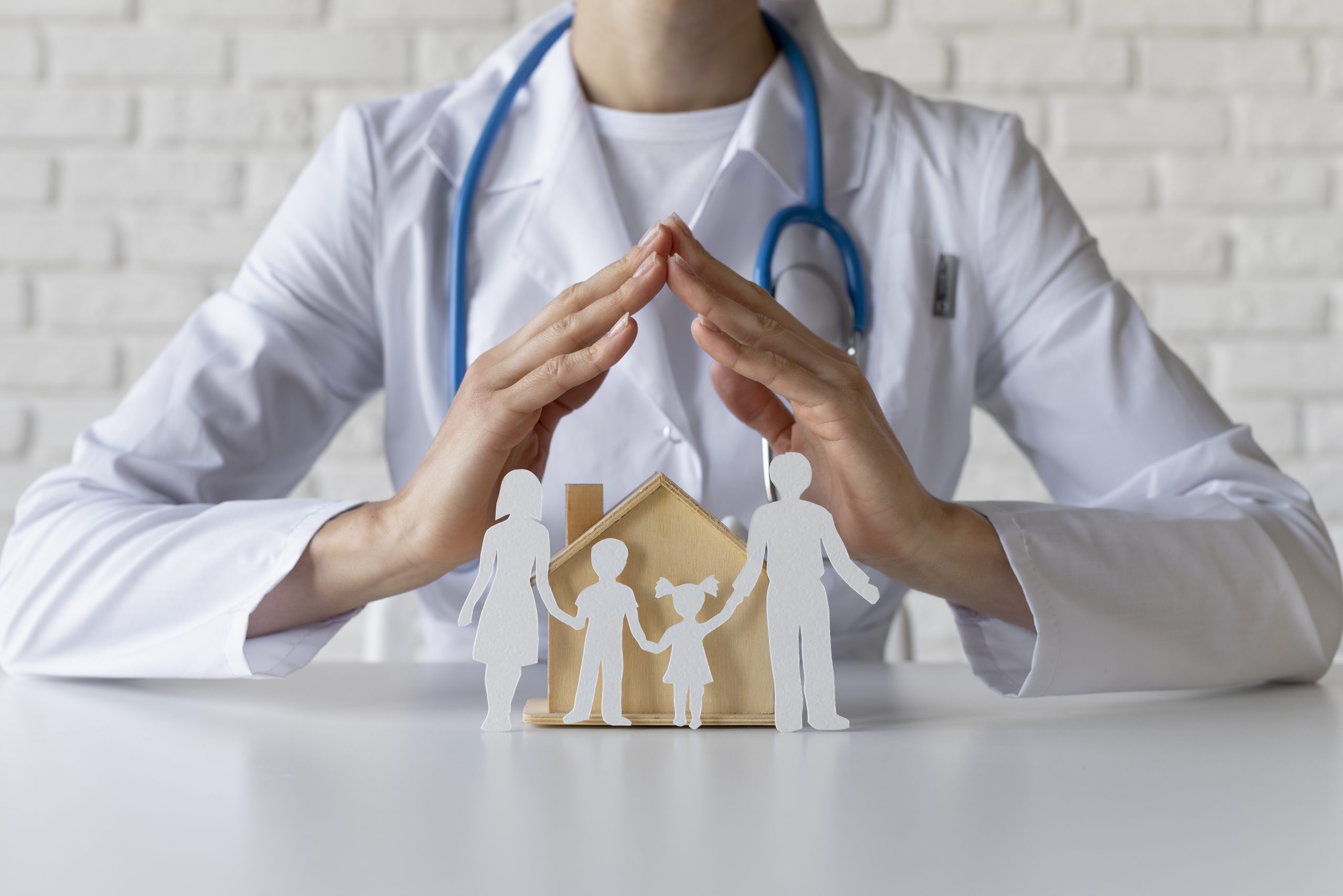 A doctor protects paper cutouts of a family and house with their hands, symbolizing healthcare, family safety, and Medicaid Asset Protection Trusts.