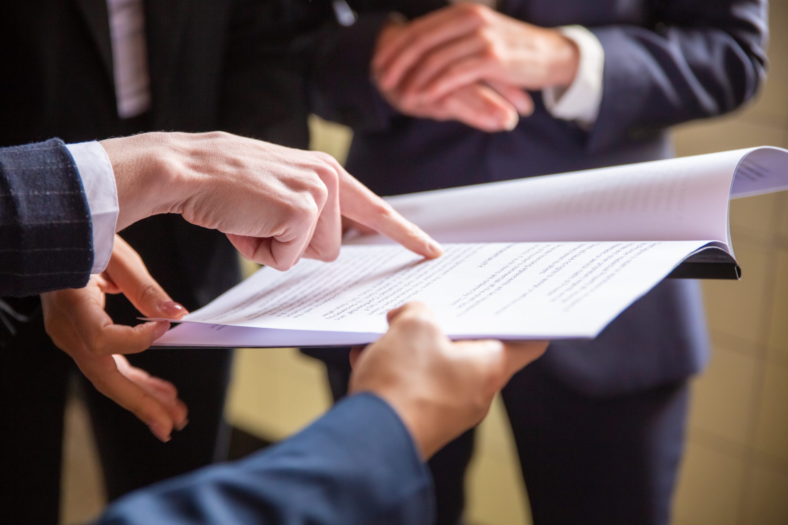 Three people in business attire review and point at documents, focusing on printed text while consulting a Power of Attorney Lawyer during a discussion.