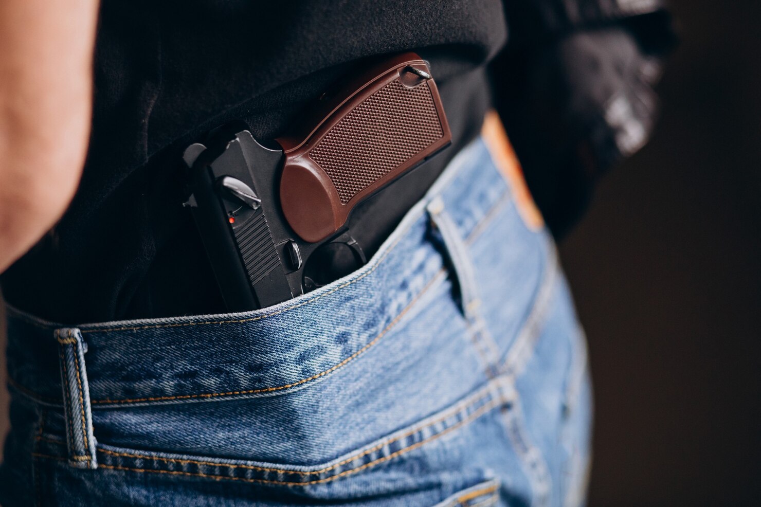A handgun in a holster is tucked into the waistband of a person wearing blue jeans and a black shirt, ready for advice from a Gun Trust Attorney.
