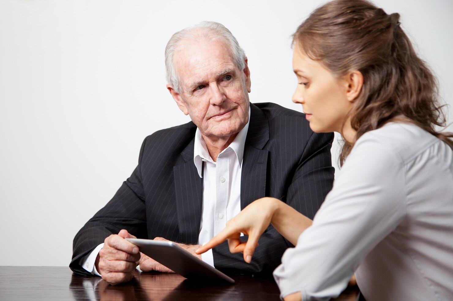 Older man in a suit listens as a younger Death Deed Attorney in business attire points at a tablet on the table between them.