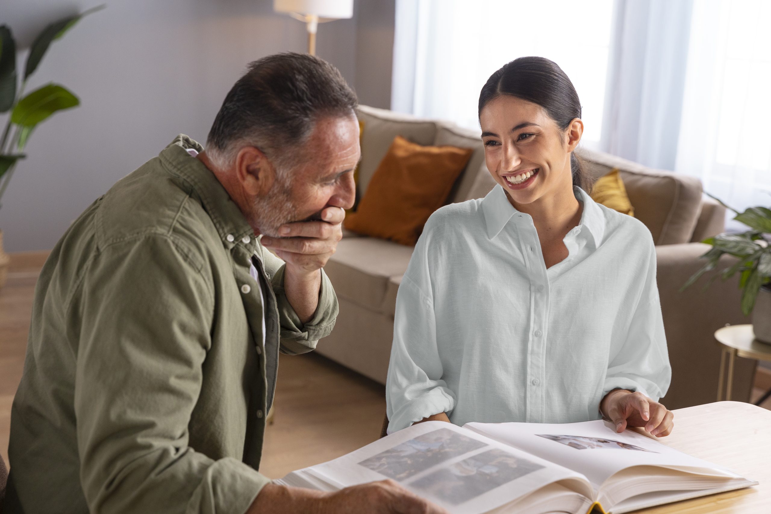 Two people sit at a table in a living room, smiling as they look at a photo album and discuss memories with guidance from an advance directive attorney.