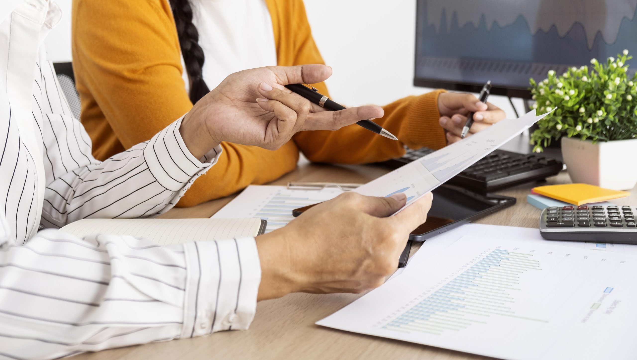 Two people sit at a desk reviewing printed charts and graphs, as a Trust Administration Attorney provides guidance with a computer and plant in the background.