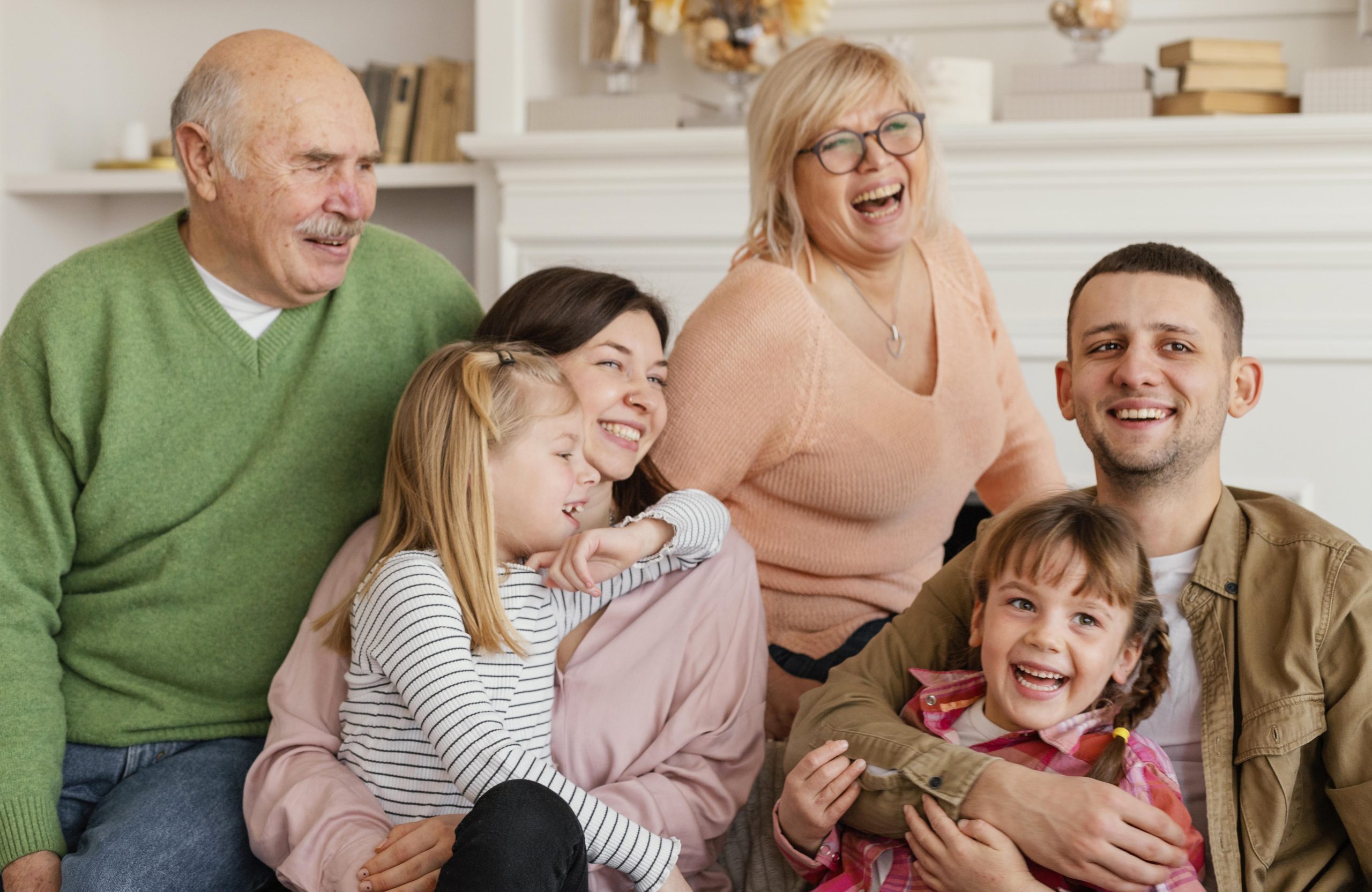 Three adults and three children sit closely together indoors, smiling and laughing, like a family guided by Ohio estate planning attorneys, in a well-lit room with shelves and a white background.